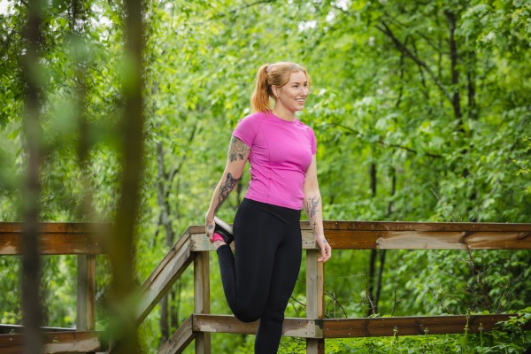 Nainen venyttelemässä aidan vieressä vihreän metsän keskellä.