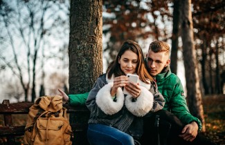 Nuori nainen ja mies luonnossa katsovat kännykkää.