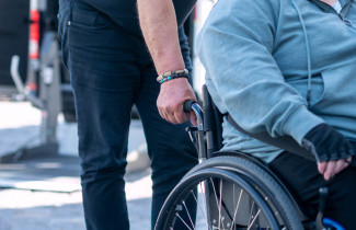 Ihminen pyörätuolissa jota toinen ihminen työntää.