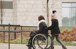 Avustaja työntää pyörätuolissa olevaa naista.