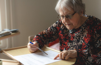 Ikääntynyt rouva täyttää lomaketta pöydän ääressä.