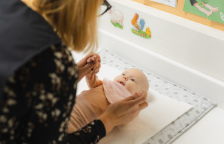 Vauva on hoitopöydällä ja katsoo terveydenhoitajaa.