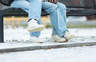 Nuoret istuvat puistonpenkillä, vain jalat näkyvät.