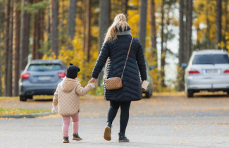 Äiti ja lapsi kävelemässä käsi kädessä parkkipaikalla.