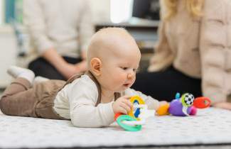 Vauva pötköttää vatsallaan lattialla ja leikkii värikkäillä leluilla.