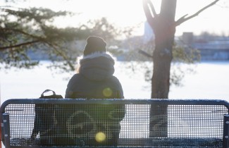 Nuori istuu puistonpenkillä talvisessa maisemassa.