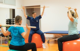 Kolme ihmistä istuu jumppapalloilla ja tekee keppijumppaa.