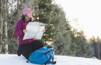 Nainen ulkoilemassa talvella, katsoo karttaa metsän reunalla.