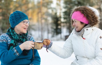 Kaksi iloista henkilöä kahvittelevat ulkona talvella.