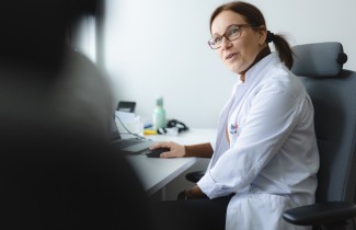 Lääkäri istuu tuolissa tietokoneen ääressä katse kohti asiakasta.