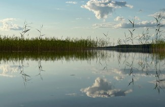 Aurinkoinen järvimaisema, jossa pilvet heijastuvat vedenpinnasta