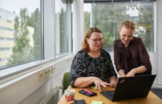 Kaksi työntekijä istuvat yhteisen tietokoneen äärellä ja katselevan tietokoneen näytölle.