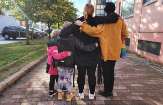 Perheenjäsenet kadulla kädet toistensa olla, takaapäin kuvattu