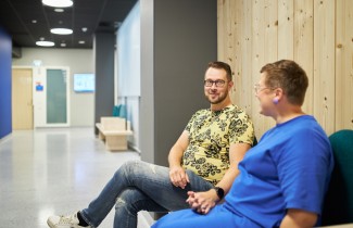 Kaksi ihmistä istuu vieretysten penkillä katsoen toisiaan kohden ja pidellen kädestä kiinni. 