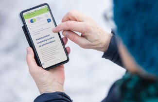 Henkilö tutkii ikääntyneen asiakasohjauksen sivuja älypuhelimella