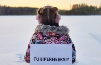 Lapsi istuu lumessa selin kameraan ja lapussa lukee Tukiperheeksi?