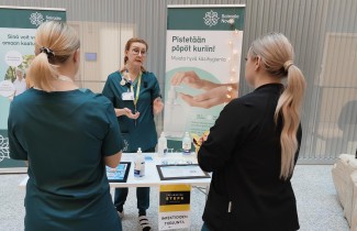 Infektiohoitaja Sari Pätsi kertoo STEPPI-päivien infektioiden torjunta -pisteellä kahdelle opiskelijalle käsihuuhteen oikeaoppisesta käytöstä. "Pistetään pöpöt kuriin!" kannustaa roll-up taustalla.