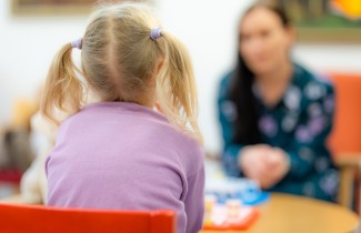 Selin kameraan istuva tyttö juttelee aikuisen kanssa