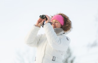 Nainen katsoo kiikareilla lumista maisemaa.