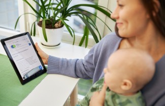 Nainen pitää vauvaa sylissä ja asioi verkkopalvelussa tabletilla