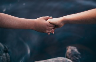 Kahden ihmiset kädet pitävät toisistaan kiinni järven yllä.