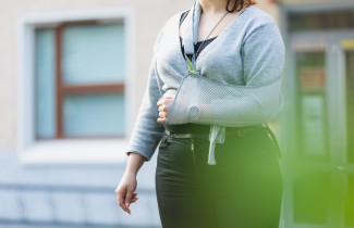 Henkilö seisoo terveyskeskuksen pihalla käsi paketissa.