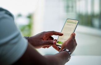 Ihminen pitää puhelinta kädessä ja selaa hyvinvointialueen Asioi verkossa -sivua.