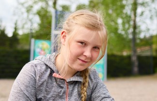 Tyttö katsoo kameraan ja taustalla näkyy leikkipuistoa