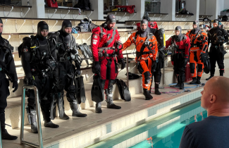 Vesisukeltajakoulutettavat sukelluspuvuissa uima-altaan reunalla