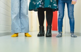 Kolme henkilöä seisoo rivissä sisätiloissa, näkyvissä vain jalat ja lattia.