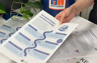 Henkilö ojentaa esitettä, jossa käsitellään omatoimista varautumista. Taustalla ämpäri, jonka kyljessä tarra, jossa lukee Kotivara