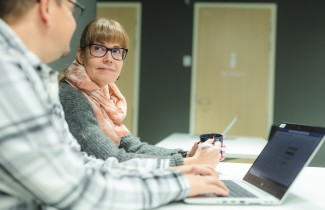 Kaksi työntekijää ovat tietokoneen ääressä ja katsovat toisiaan hymyillen.