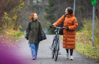 Kaksi naista kävelevät syksyisellä kadulla ja katsovat toisiinsa.