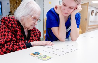 Ikääntynyt ja opiskelija pelaavat muistipeliä.