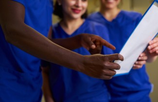 Kolme hoitaja-asuista henkilöä tarkastelee yhden käsissä olevaa dokumenttia.