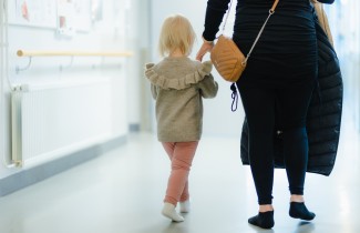 Pieni lapsi ja aikuinen kävelevät käytävällä, lapsi pitää aikuisen kädestä kiinni.