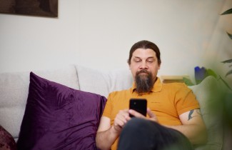 Parrakas henkilö istuu mukavasti sohvalla ja selaa puhelinta.