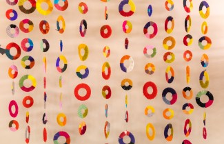 Värikkäitä koristeita roikkuu nauhoissa rinnakkain vaalealla taustalla.