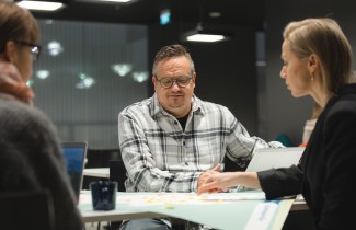 Kolme henkilöä istuu pöydän ääressä. Pöydällä on karttakuva Keski-Suomesta, jota yksi osoittaa sormellaan.
