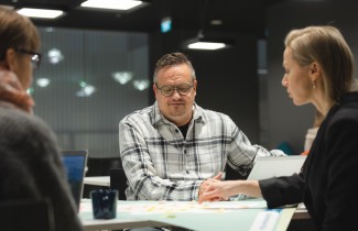 Kolme henkilöä istuu pöydän ääressä. Pöydällä on karttakuva Keski-Suomesta, jota yksi osoittaa sormellaan.