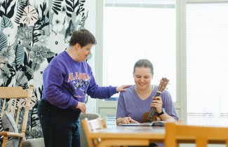 Yksi henkilö soittaa ukulelea ja toinen henkilö laulaa.