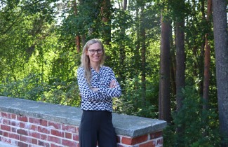 Tiina Föhr seisoo hymyilevänä Jyväskylän yliopiston kampuksella vehreän metsän ja aidan vieressä.