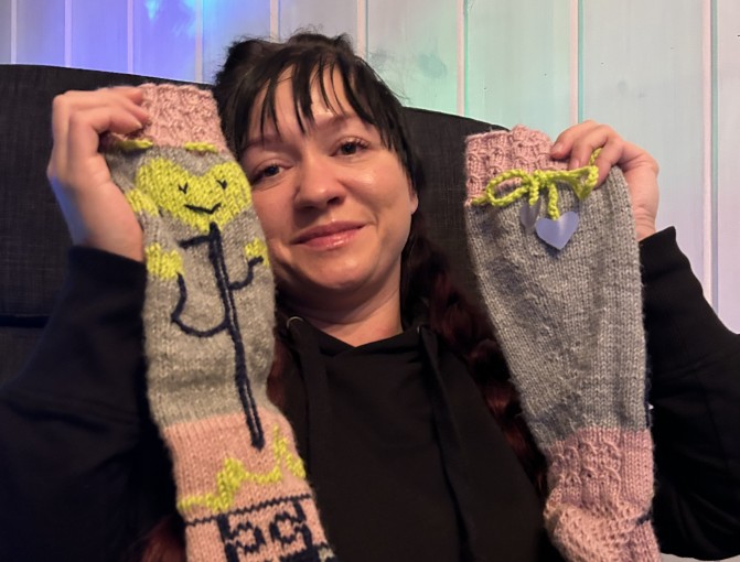 Tanja Viinikainen pitelee tekemiään Läsnäolo-sukkia, joissa kuviona on puun runkoa ja palapeliä. Varsiin on kiinnitetty heijastimet.