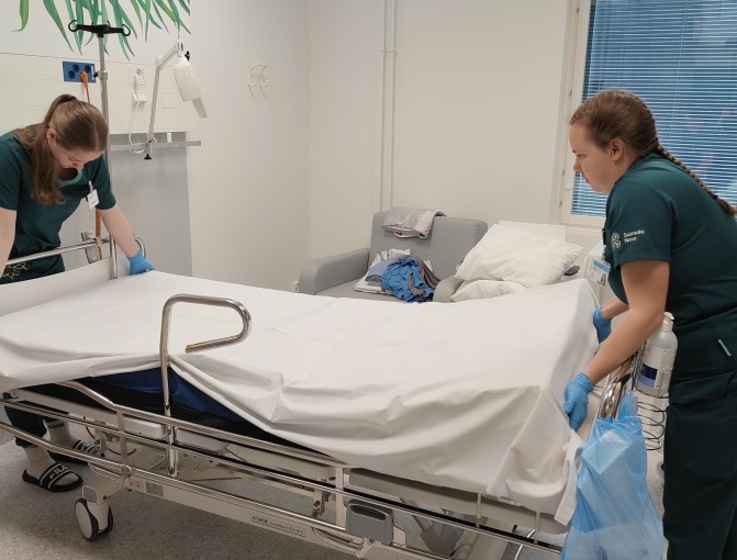 STEPPI-agentti Esteriina Hertteli opastaa opiskelijaa sängyn petaamisessa. Potilassänkyyn laitetaan lakanaa pää- ja jalkopäästä yhteistyössä.