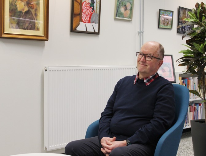 Mies istuu nojatuolissa hymyillen.