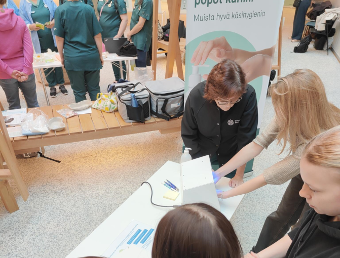 Infektiotorjuntapisteellä opiskelijat harjoittelevat käsihuuhteen käyttöä. Käsien puhtaus todennetaan sinivalolaitteella, joka näyttää, mihin huuhde on yltänyt.