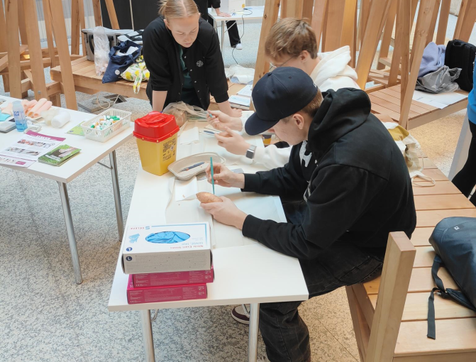 Kaksi opiskelijaa harjoittelee kovettumien poistoa bataatin pinnasta. Ammattilainen seuraa.