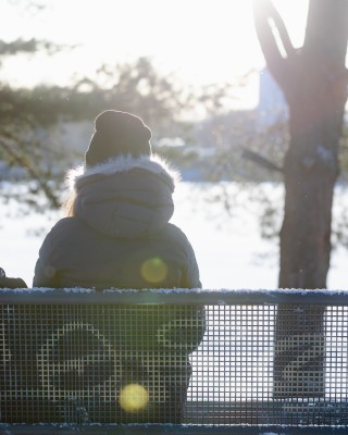 Nuori istuu puistonpenkillä talvisessa maisemassa.