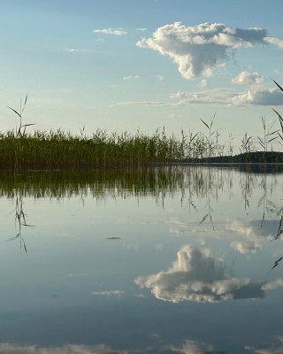 Aurinkoinen järvimaisema, jossa pilvet heijastuvat vedenpinnasta