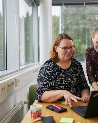 Kaksi työntekijä istuvat yhteisen tietokoneen äärellä ja katselevan tietokoneen näytölle.